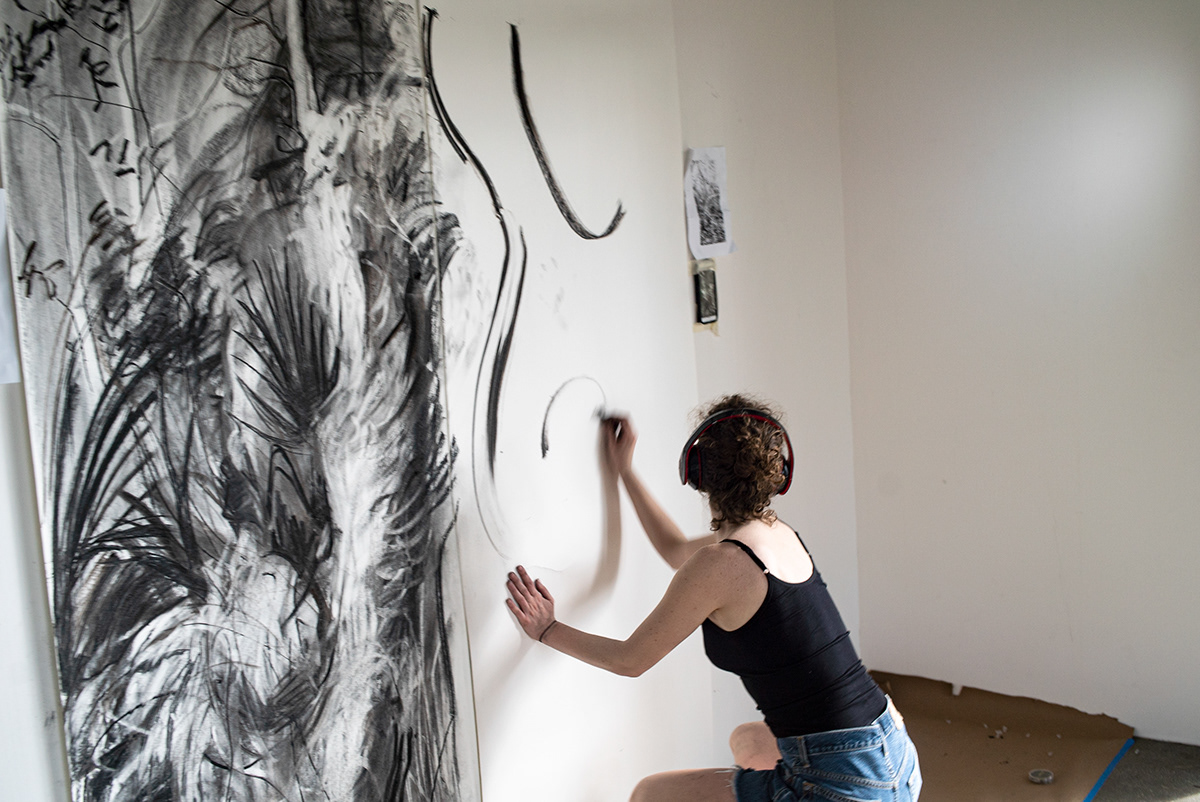 The artist, Rachel Gray, crouches with charcoal in hand as she works on her large-scale drawing.