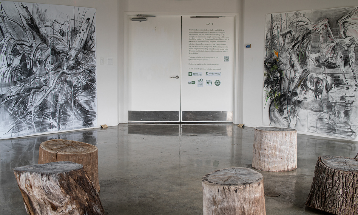 View of the exhibition Connections and Alliances in the Nest Gallery. On either side of the entrance doors there are large-scale charcoal drawings.